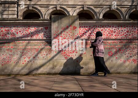 Londra, Regno Unito. 4 aprile 2021. Una donna vede i cuori la domenica di Pasqua su un muro a Lambeth, vicino al Tamigi, con ogni cuore che rappresenta qualcuno che è morto durante la pandemia di coronavirus in corso nel Regno Unito. Chiamato il National Covid Memorial Wall, è stato creato dal gruppo chiamato Covid-19 famiglie in lutto per la giustizia con il lavoro che inizia una settimana fa e si estende per mezzo miglio per il momento in cui è completo. Credit: Stephen Chung / Alamy Live News Foto Stock