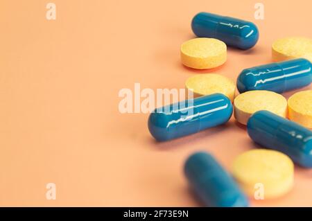 Pillole arancioni e capsule blu su sfondo di pesca con spazio per il testo. Immagine della medicina. Assistenza sanitaria. Foto Stock