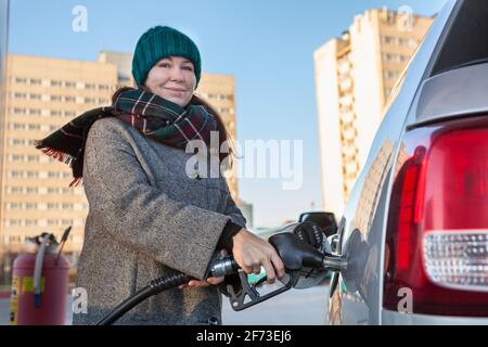 Donna attraente che trattiene l'ugello della pompa di alimentazione con il rifornimento di gasolio la sua auto al distributore di benzina urbano self-service Foto Stock