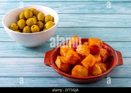 Concetto di gastronomia spagnola. Piatto di argilla con patate fritte con salsa piccante chiamata in Spagna 'Patatas Bravas' con una ciotola bianca di oliv ripieno Foto Stock