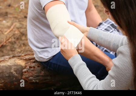 Giovane donna che applica il bendaggio sul braccio dell'uomo maturo nella foresta Foto Stock