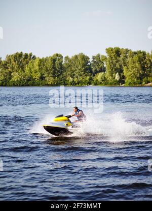 L'uomo forte salta sul jetski sopra l'acqua. Uomo che accelera su moto d'acqua sul lago durante le vacanze estive Foto Stock