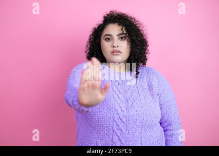 Giovane bella donna che indossa un maglione casual su sfondo rosa isolato serio e facendo smettere di cantare con palmo della mano. Foto Stock