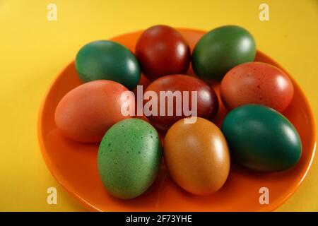 Colorate uova di pasqua dipinte su piatto arancione primo piano su sfondo giallo, symbool di primavera Foto Stock