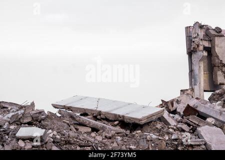 Una lastra grigia di cemento si trova sulla cima di un mucchio di macerie contro i resti di un edificio e il cielo grigio. Sfondo. Foto Stock