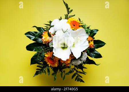 Bouquet con fiori bianchi e arancioni e foglie verdi su sfondo giallo. Foto Stock