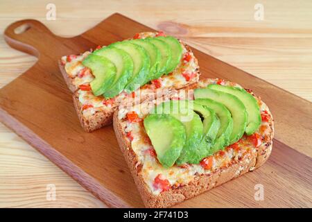 Preparare un paio di toast fatti in casa alla griglia con un condimento pomodoro e avocado su una tavola di pane Foto Stock