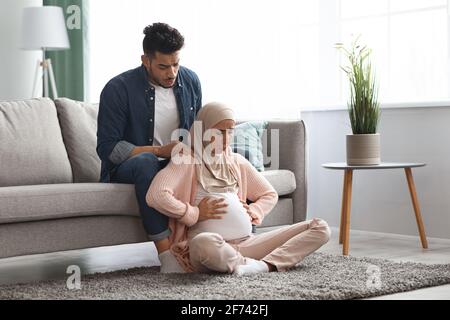 Donna musulmana incinta che soffre di contrazioni prenatali a casa, marito premuroso che la conforta Foto Stock