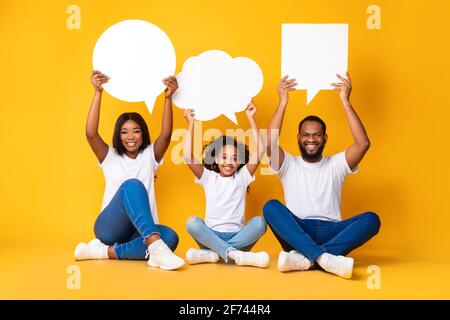 Sorridente famiglia nera che si accoviglia bolle di parole in studio Foto Stock