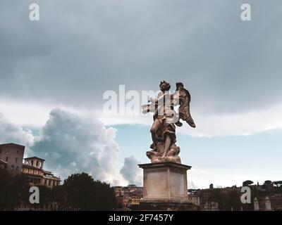 Roma, Italia - 18 agosto 2019: Antica scultura in marmo sul Ponte Sant'Angelo attraverso il fiume Tevere su epico sfondo panoramico del cielo. Colore classificato Foto Stock