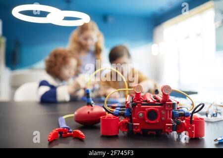 Primo piano della macchina robot rossa sul tavolo in classe di ingegneria con bambini in background, spazio di copia Foto Stock