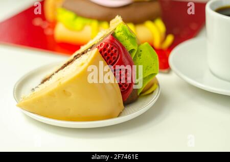 Pezzo della torta Burger, Madeira e torta stratificata di spugna di cioccolato, riempito con glassa ricoperta di glassa morbida e decorazioni di zucchero commestibile, torta i Foto Stock