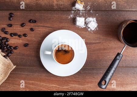 Immagine a pianta piatta con vista dall'alto che mostra il tradizionale caffè turco servito in tazze classiche con delizie turche. Sullo sfondo è presente una caffettiera in metallo. Foto Stock