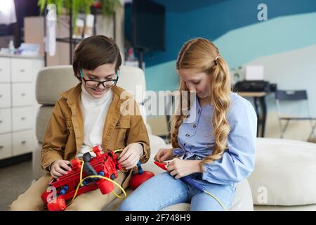 Ritratto di due bambini che giocano con la macchina robotica durante la lezione di ingegneria in interni della scuola moderna, copy space Foto Stock
