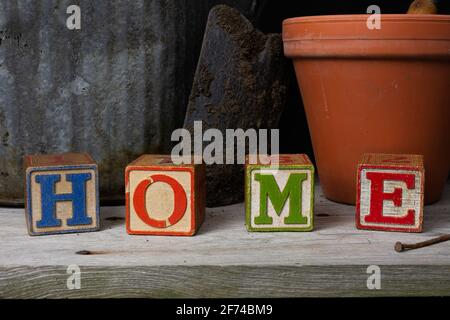 'Home' scritto in blocchi di legno d'epoca con sfondo giardinaggio. Foto Stock