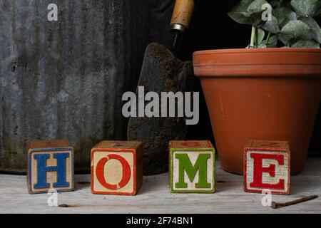 'Home' scritto in blocchi di legno d'epoca con sfondo giardinaggio. Foto Stock