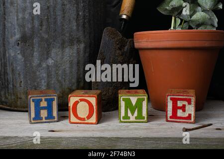 'Home' scritto in blocchi di legno d'epoca con sfondo giardinaggio. Foto Stock