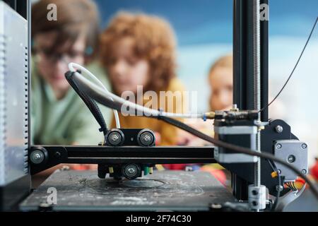 Primo piano della produzione di modelli in plastica da parte di stampanti 3D durante la lezione di ingegneria e robotica a scuola con bambini in background, copy space Foto Stock