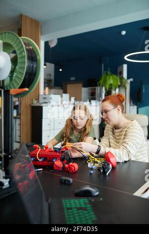 Ritratto verticale della giovane insegnante che aiuta la ragazza a costruire robot durante la lezione di ingegneria alla scuola moderna Foto Stock