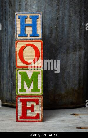 'Home' scritto in blocchi di legno vintage con arrugginito annaffiatura può sfondo. Foto Stock