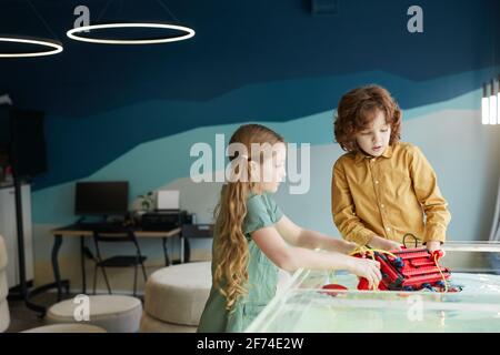 Ritratto di due bambini che mettono robo in acqua mentre sperimentano la tecnologia al laboratorio di robotica a scuola, copia spazio Foto Stock