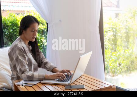 Donna asiatica che lavora con il computer portatile. Donna d'affari impegnata a lavorare su un computer portatile a casa. Donna asiatica freelance online che lavora con il laptop. Business An Foto Stock