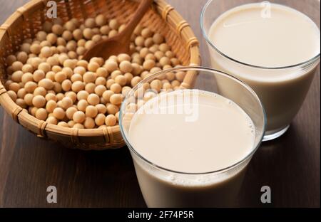 Latte di soia in un bicchiere su sfondo di legno. Fagioli di soia in un colander di bambù sullo sfondo Foto Stock