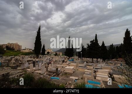 tzfat-israele. 22-03-2021. Veduta dall'alto delle tombe affollate, nel nuovo cimitero della città di Tzfat, sullo sfondo di un cielo invernale nuvoloso Foto Stock