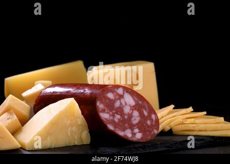 Diversi tipi di formaggio giallo a pezzi e tagliato a fette e pezzo di pane di salame sono su tavola di pietra nera su sfondo scuro. Preparazione del chee Foto Stock