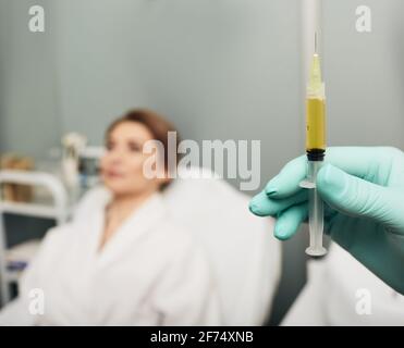 Siringa con plasma sanguigno di un paziente in una mano di un cosmetologo per un plasmolifting della pelle di una donna. Plasma terapia, il ripristino delle cellule della pelle Foto Stock