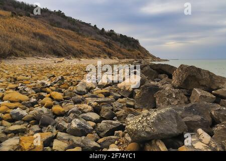 Vista sulla spiaggia con pietre scure in primo piano nella stagione invernale. Pesaro, Regione Marche, Italia Foto Stock