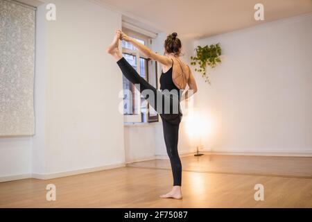 Vista laterale di una donna anonima flessibile a piedi nudi che esegue la posizione estesa Mano alla convergenza posare sul pavimento contro la lampada luminosa Foto Stock