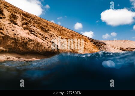 Basso angolo di acque marine limpide lavando scogliera rocciosa sulla costa sotto il cielo blu con le nuvole Foto Stock