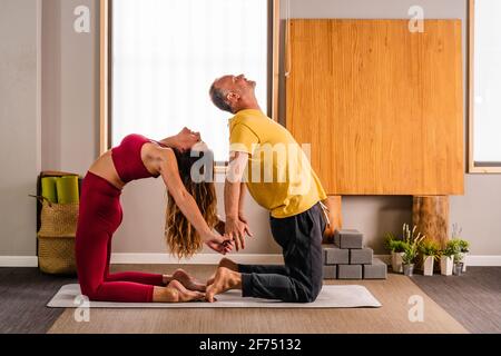 Vista laterale della coppia calma in abbigliamento sportivo che esegue l'esercizio Ustrasana mentre si pratica yoga in studio alla luce del giorno Foto Stock