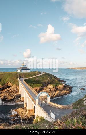 Spettacolare scenario di ponte che conduce a un'isola rocciosa coperta da Erba verde con faro posto in oceano ondulato a Faro Illa Pancha in Galizia in Foto Stock
