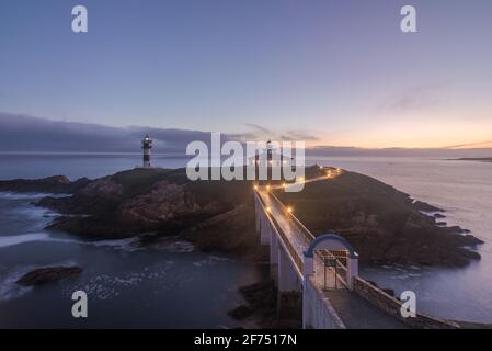 Spettacolare scenario di ponte che conduce a un'isola rocciosa coperta da Erba verde con faro posto in oceano ondulato a Faro Illa Pancha in Galizia in Foto Stock