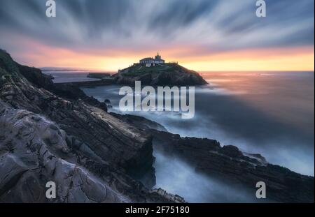 Scenario mozzafiato di isola rocciosa con faro situato in oceano Vicino costa rocciosa a Faro Tapia de Casariego nelle Asturie In Spagna sotto la nuvolosa sk Foto Stock