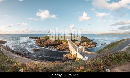 Spettacolare scenario di ponte che conduce a un'isola rocciosa coperta da Erba verde con faro posto in oceano ondulato a Faro Illa Pancha in Galizia in Foto Stock