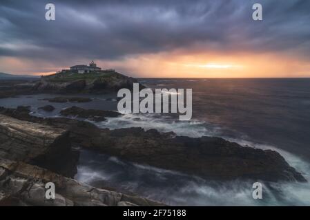 Scenario mozzafiato di isola rocciosa con faro situato in oceano Vicino costa rocciosa a Faro Tapia de Casariego nelle Asturie In Spagna sotto la nuvolosa sk Foto Stock