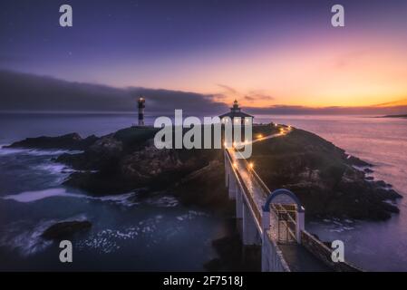 Spettacolare scenario di ponte che conduce a un'isola rocciosa coperta da Erba verde con faro posto in oceano ondulato a Faro Illa Pancha in Galizia in Foto Stock