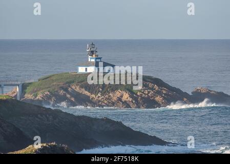 Spettacolare scenario di ponte che conduce a un'isola rocciosa coperta da Erba verde con faro posto in oceano ondulato a Faro Illa Pancha in Galizia in Foto Stock