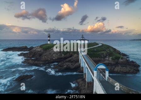Spettacolare scenario di ponte che conduce a un'isola rocciosa coperta da Erba verde con faro posto in oceano ondulato a Faro Illa Pancha in Galizia in Foto Stock