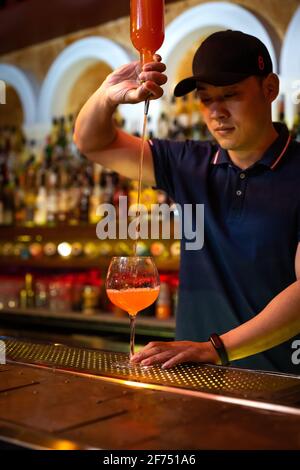 Giovane barista asiatico che versa succo di pompelmo nel bicchiere preparazione di un cocktail al bar Foto Stock