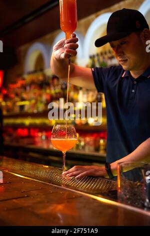 Giovane barista asiatico che versa succo di pompelmo nel bicchiere preparazione di un cocktail al bar Foto Stock