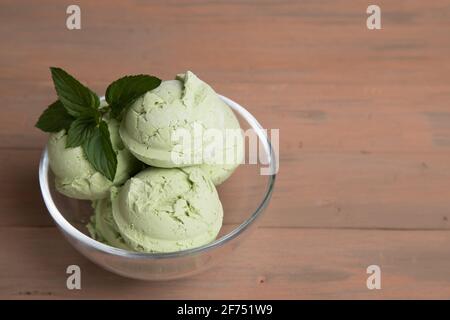 Tazza di vetro con palle di gelato al tè verde matcha su sfondo di legno. Foto Stock