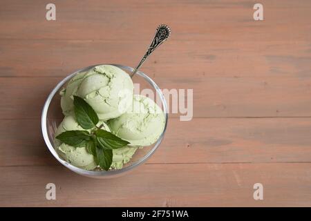 Tazza trasparente con palle di gelato al tè verde matcha su sfondo di legno. Foto Stock