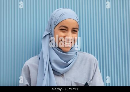 Giovane donna musulmana solitaria con uno sguardo malinconico che guarda la macchina fotografica contro le pareti a coste durante il giorno Foto Stock