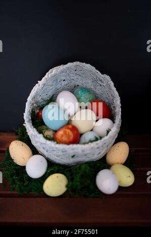 Uova di Pasqua colorate in cesto di vimini su sfondo nero Foto Stock