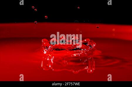 Corona d'acqua formata da uno spruzzi circolare in modalità macro in un contenitore rosso con fondo nero superiore. Foto Stock