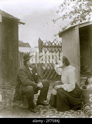 Donna vittoriana e l'uomo condividono uno scherzo dietro la capanna di vasellatura (c.. 1900) – tuttavia sembra minacciarlo con una cazzuola! La sede è Gloucestershire, Inghilterra, Regno Unito. Foto Stock